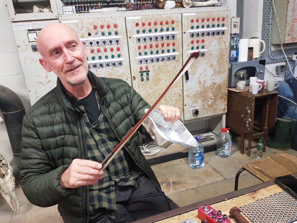 Sören Runolf is holding a bow and a metal container, with control panels in the background.