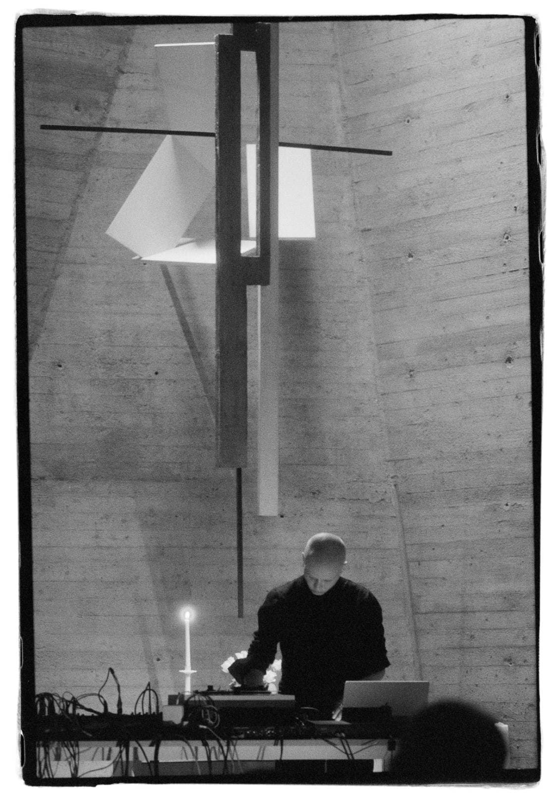 A person is standing at a table with electronic equipment and a lit candle, in a minimalist space with modern art on the wall.