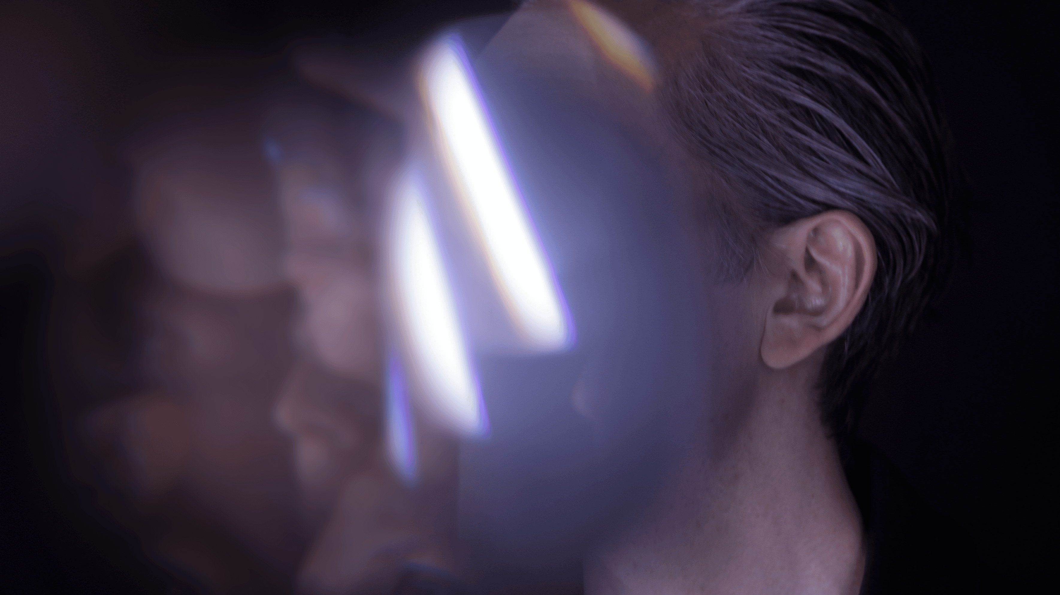 A person with slicked-back hair is partially obscured by lens flares and reflections, creating a distorted and abstract effect.