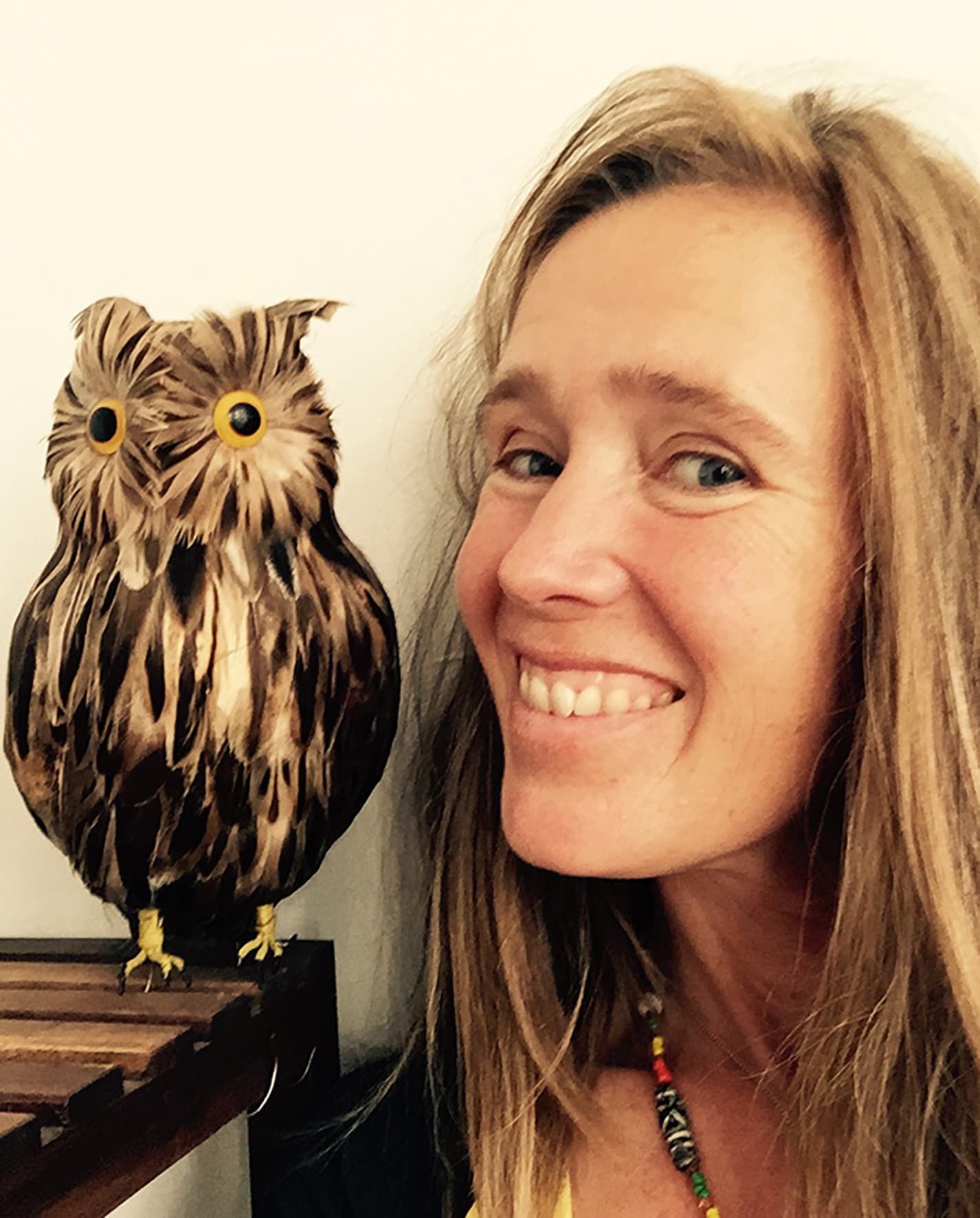 A woman smiling next to a realistic owl sculpture.