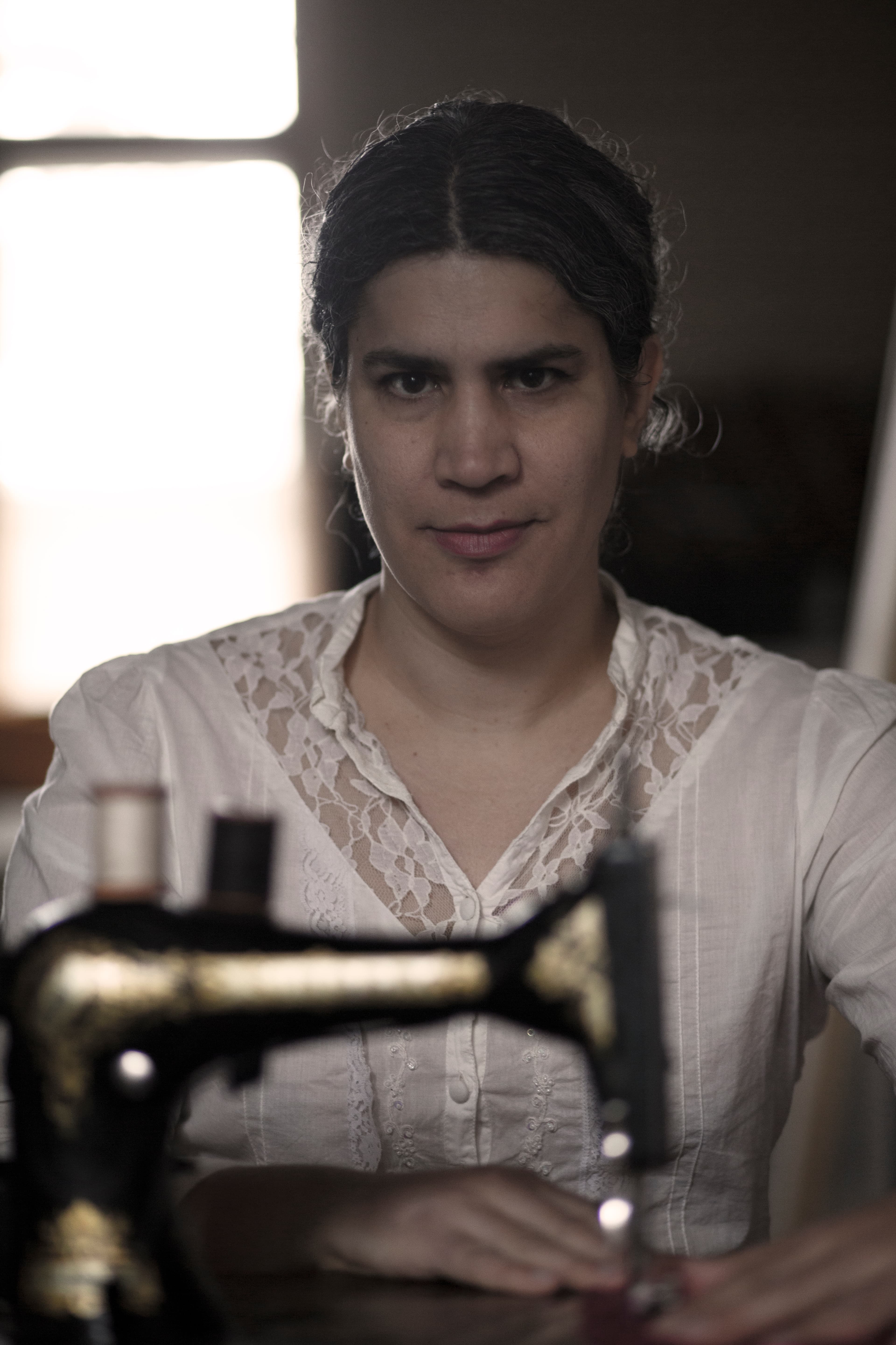A person in a vintage white blouse sits behind an antique sewing machine.
